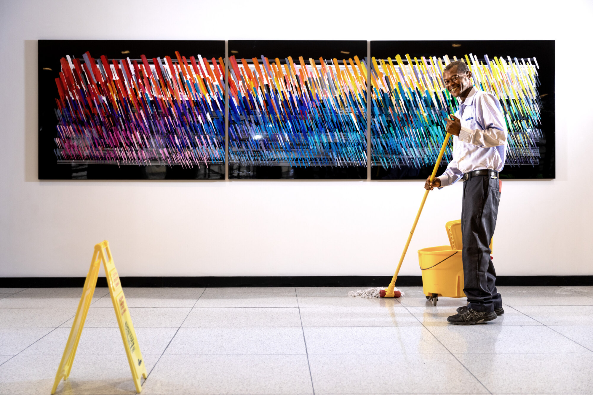 A person mopping the floor in front of a colorful abstract artwork in a gallery.